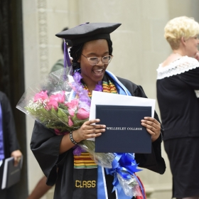 After the ceremony, a student stands on the steps of Clapp Library, clutching her diploma and a bunch of flowers.