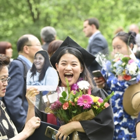 A laughing graduate clutches her flowers and diploma.