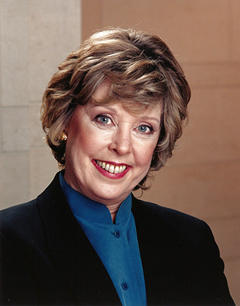 Formal portrait of Betsy smiling and wearing a suit jacket indoors