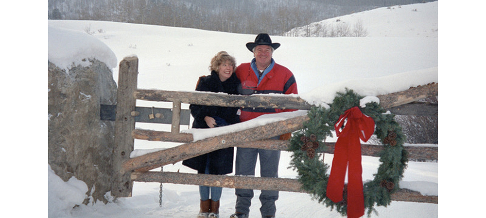 贝特西和Bud in front of a snowy landscape and behind a gate with a Christmas wreath