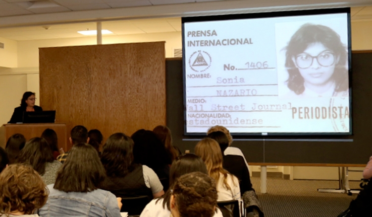 记者索尼娅·纳扎里奥(Sonia Nazario)对一屋子学生讲话。投影仪上有一张她的记者证图片。