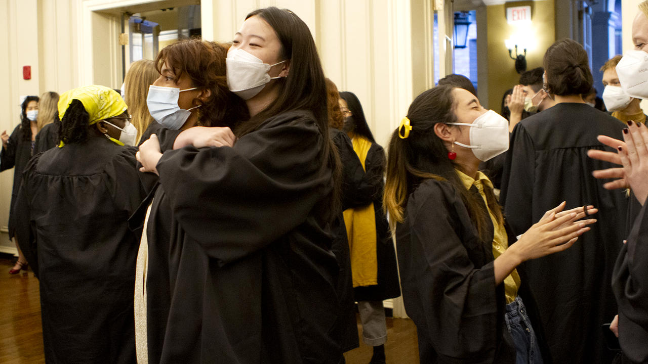 毕业典礼前，穿着长袍、戴着口罩的高年级学生聚在一起欢笑拥抱。