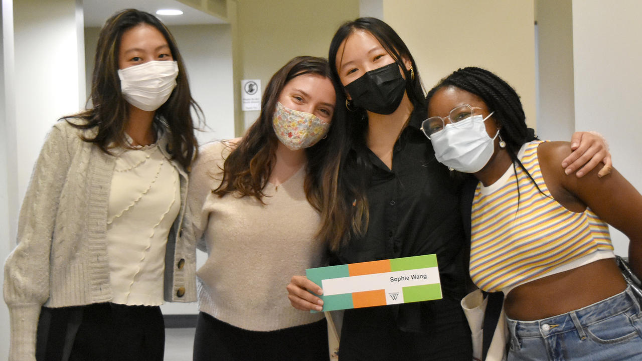 Four students stand arm in arm with one holding a Tanner sign in front of her.